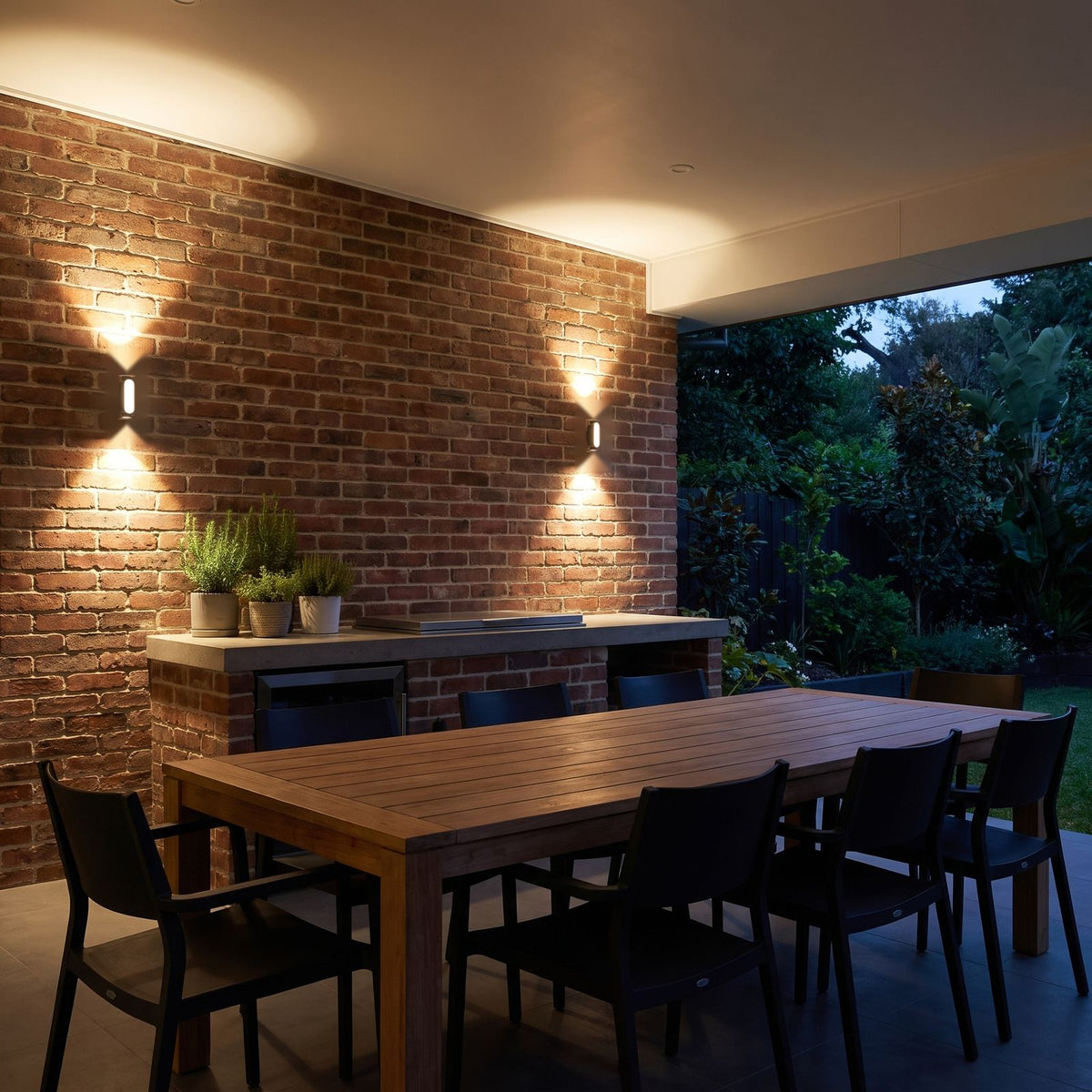 Oval Up Down Acrylic Outdoor Wall Lights on the brick wall of an alfresco dining area in the evening