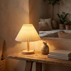 Pleated Shade Solid Wood Bedside Table Lamp glowing on a timber shelf at dusk