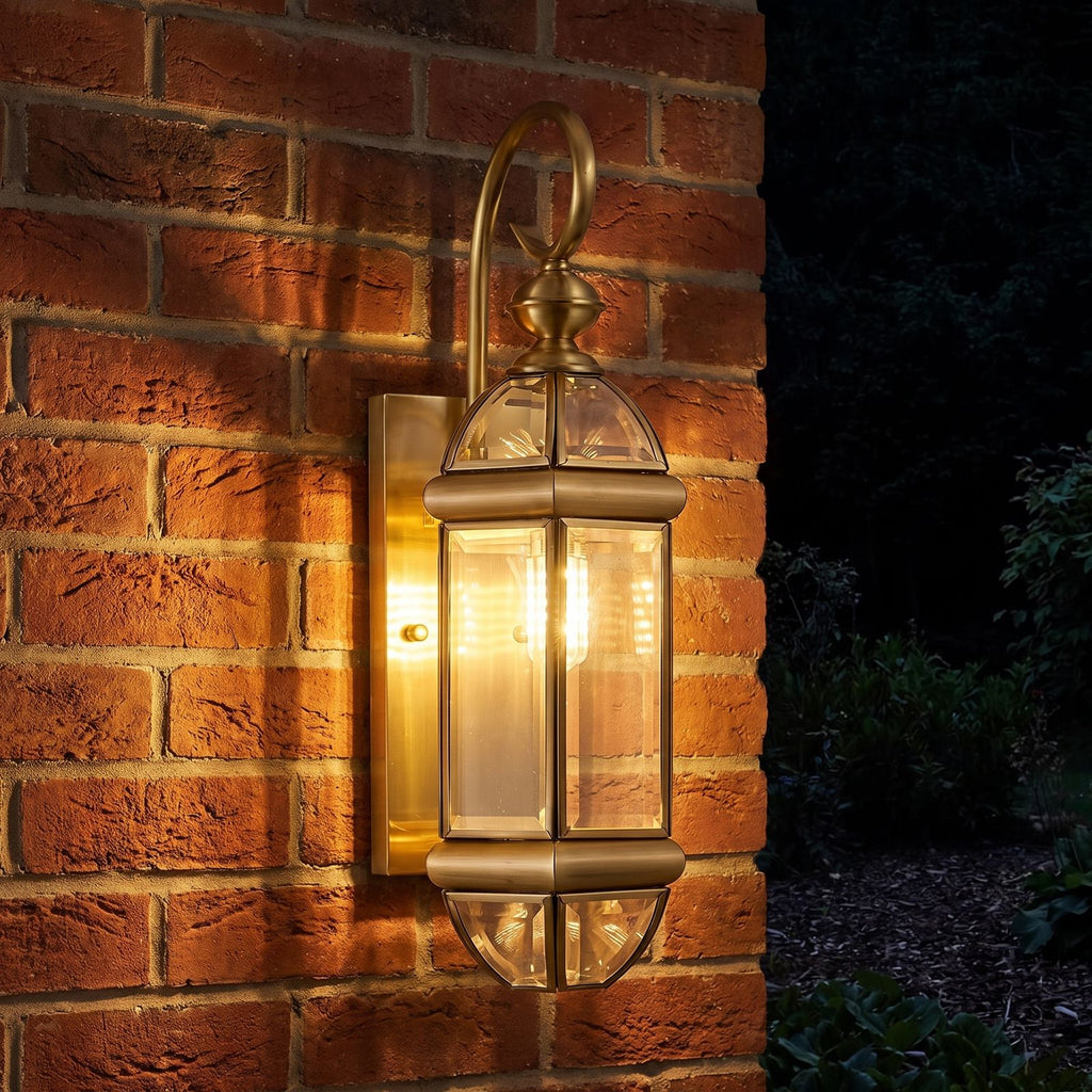 Polished Brass Clear Glass Outdoor Wall Light glowing on a garden wall at night