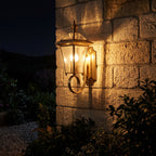 Polished Brass Coastal Outdoor Wall Lantern glowing on a garden wall at night