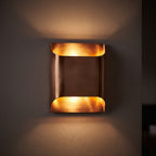 Polished Copper Double LED Wall Light glowing on a plaster wall at night