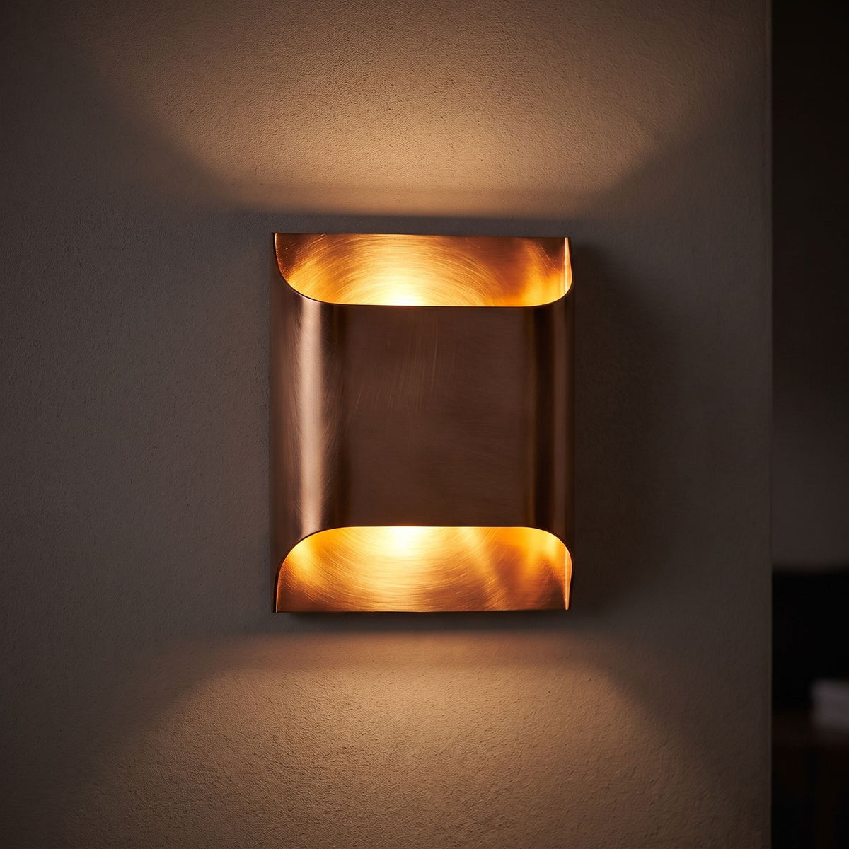Polished Copper Double LED Wall Light glowing on a plaster wall at night