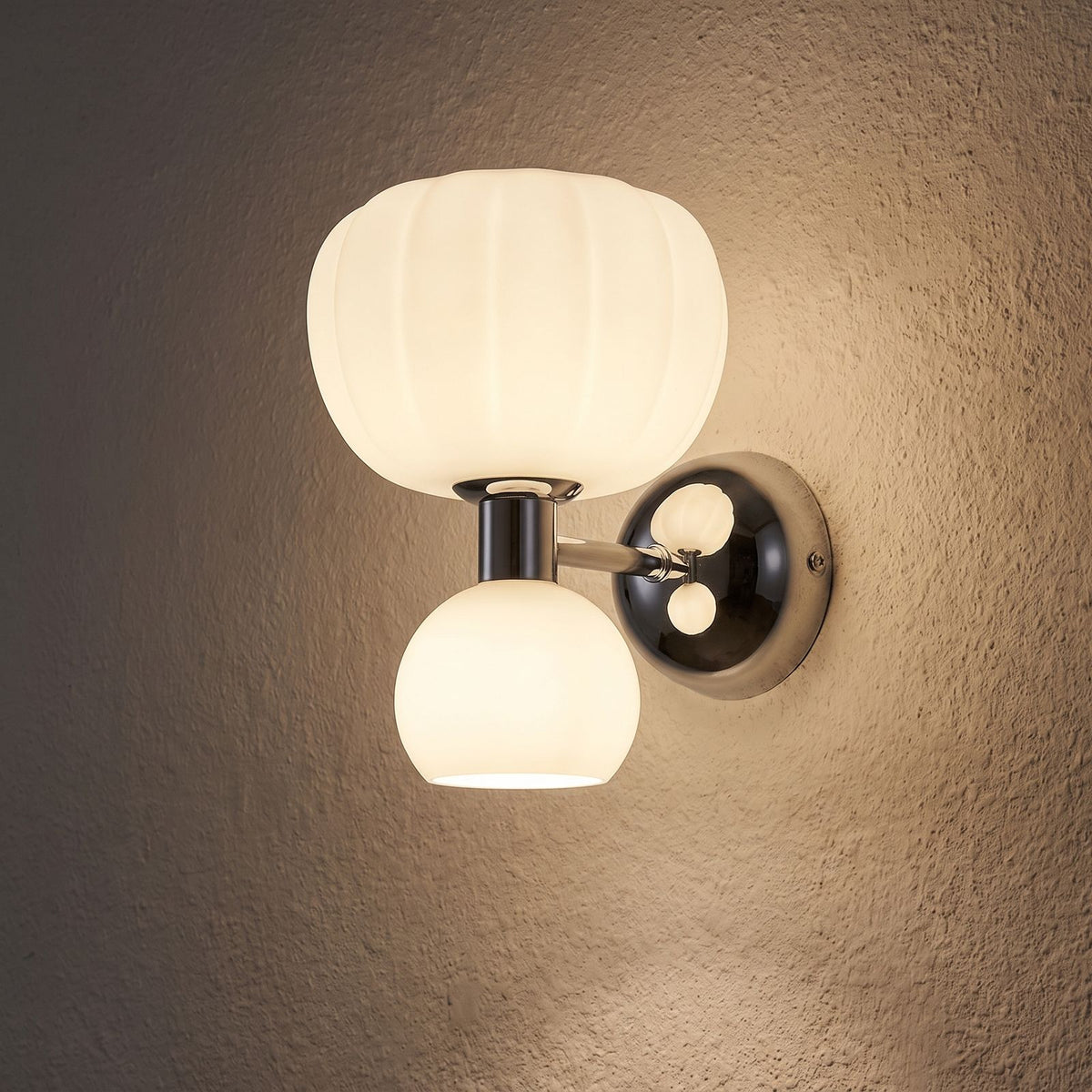 Pumpkin Shade Chrome Wall Sconce glowing on a plaster wall at night