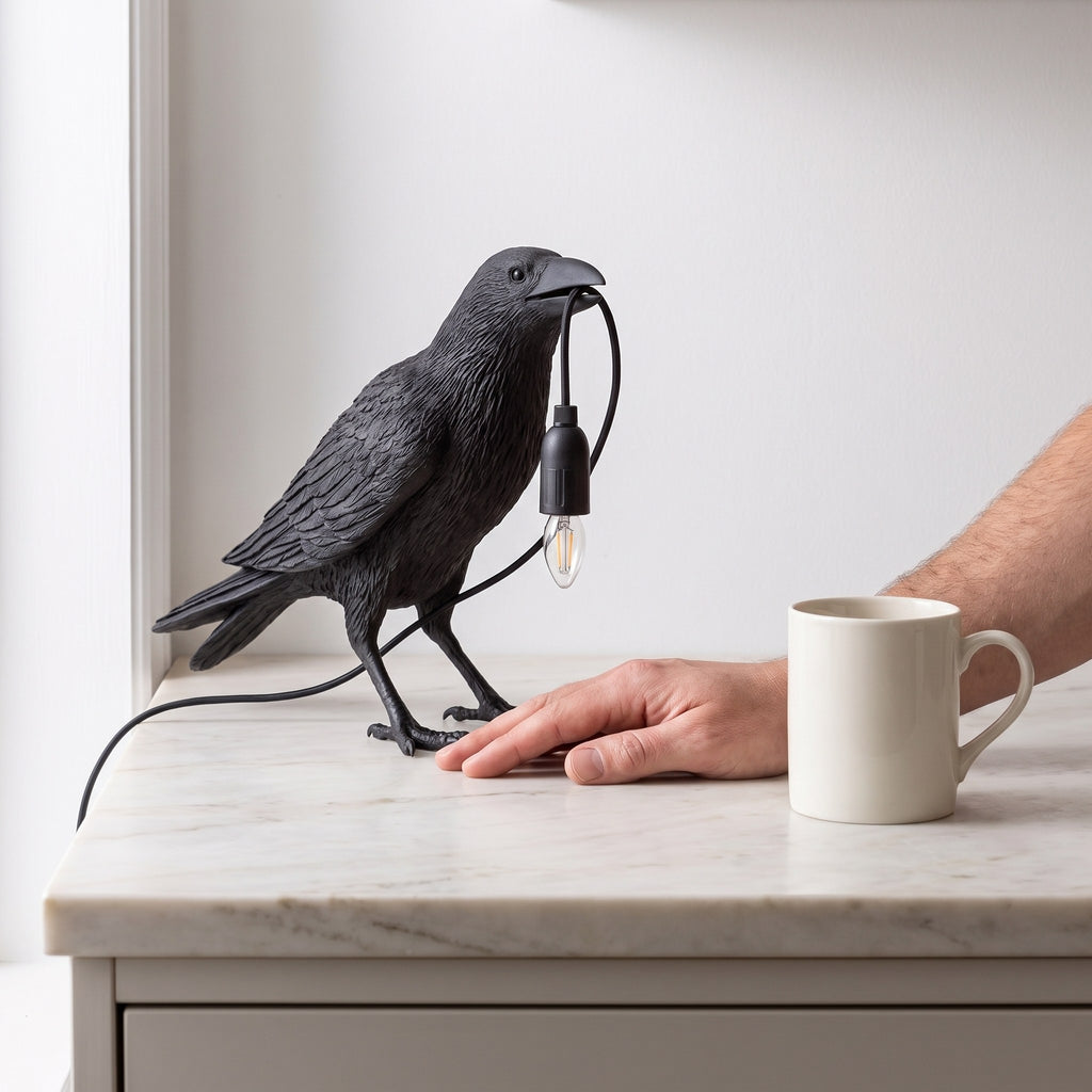 Raven Sculpture Resin Table Lamp beside a hand and a coffee mug, showing its size