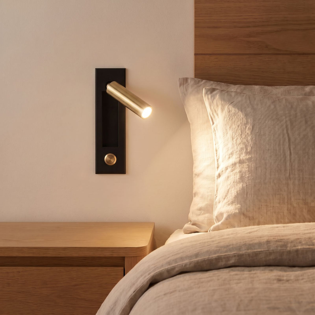 Recessed Swivel Tube Bedside Reading Wall Light in matte black and brass beside a bed
