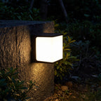 Rectangular Acrylic Solar Outdoor Wall Light glowing on a garden wall at night