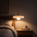 Ribbed disc and matte glass pendant light over a bedside table at night