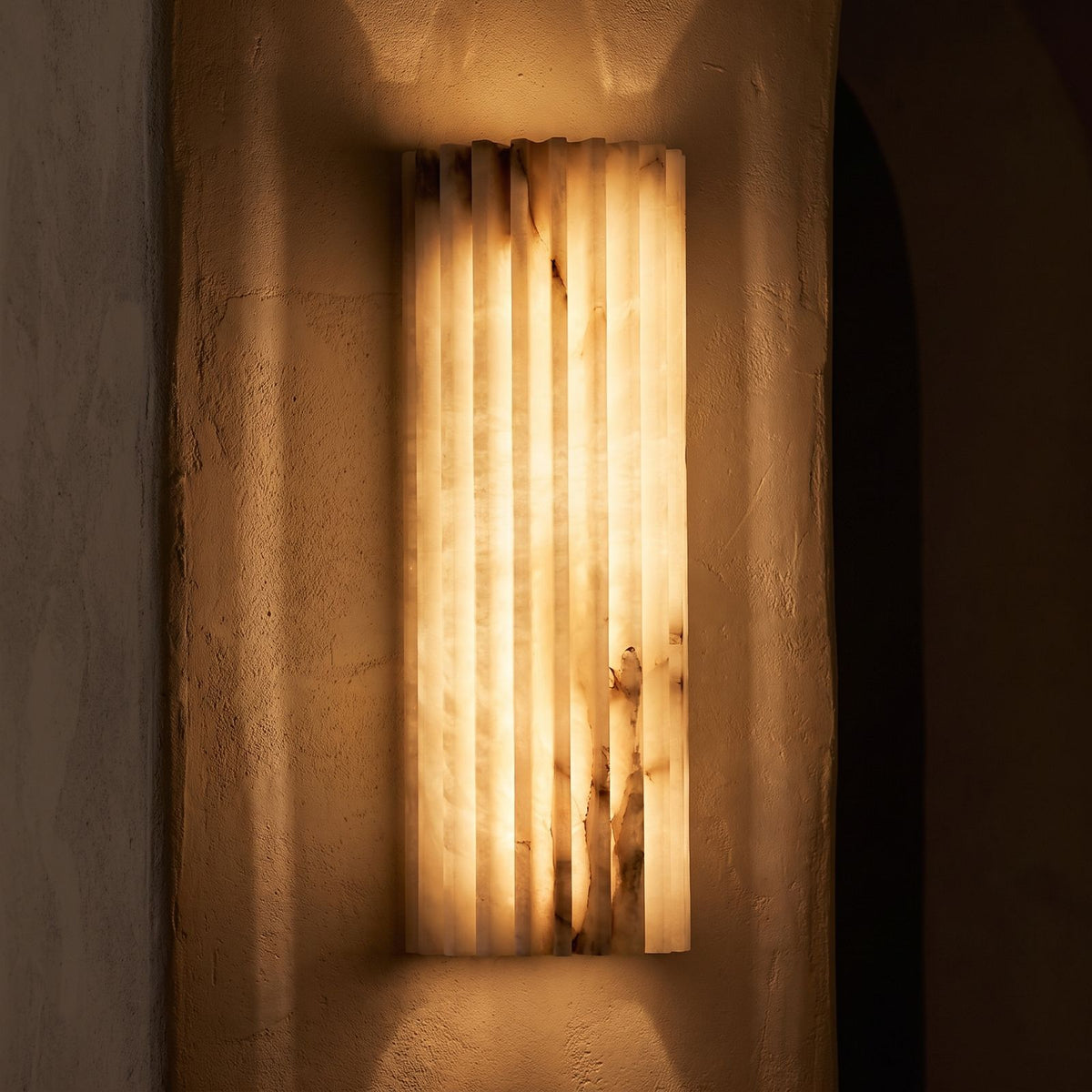 Ribbed Alabaster Column LED Wall Light glowing on a plaster wall at night