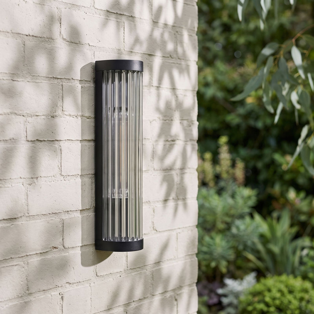 Ribbed Glass Cylinder Outdoor Wall Light on a painted brick wall, angled close view