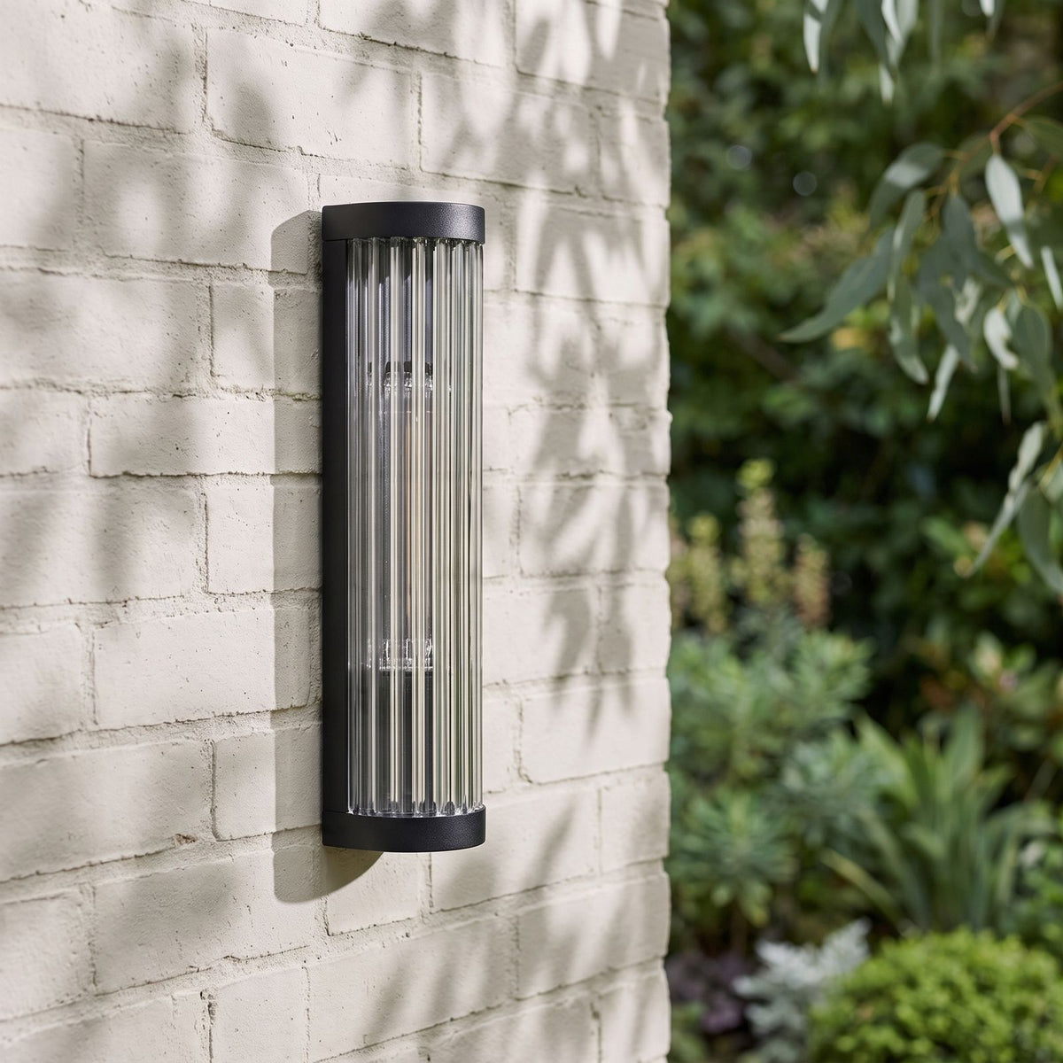 Ribbed Glass Cylinder Outdoor Wall Light on a painted brick wall, angled close view