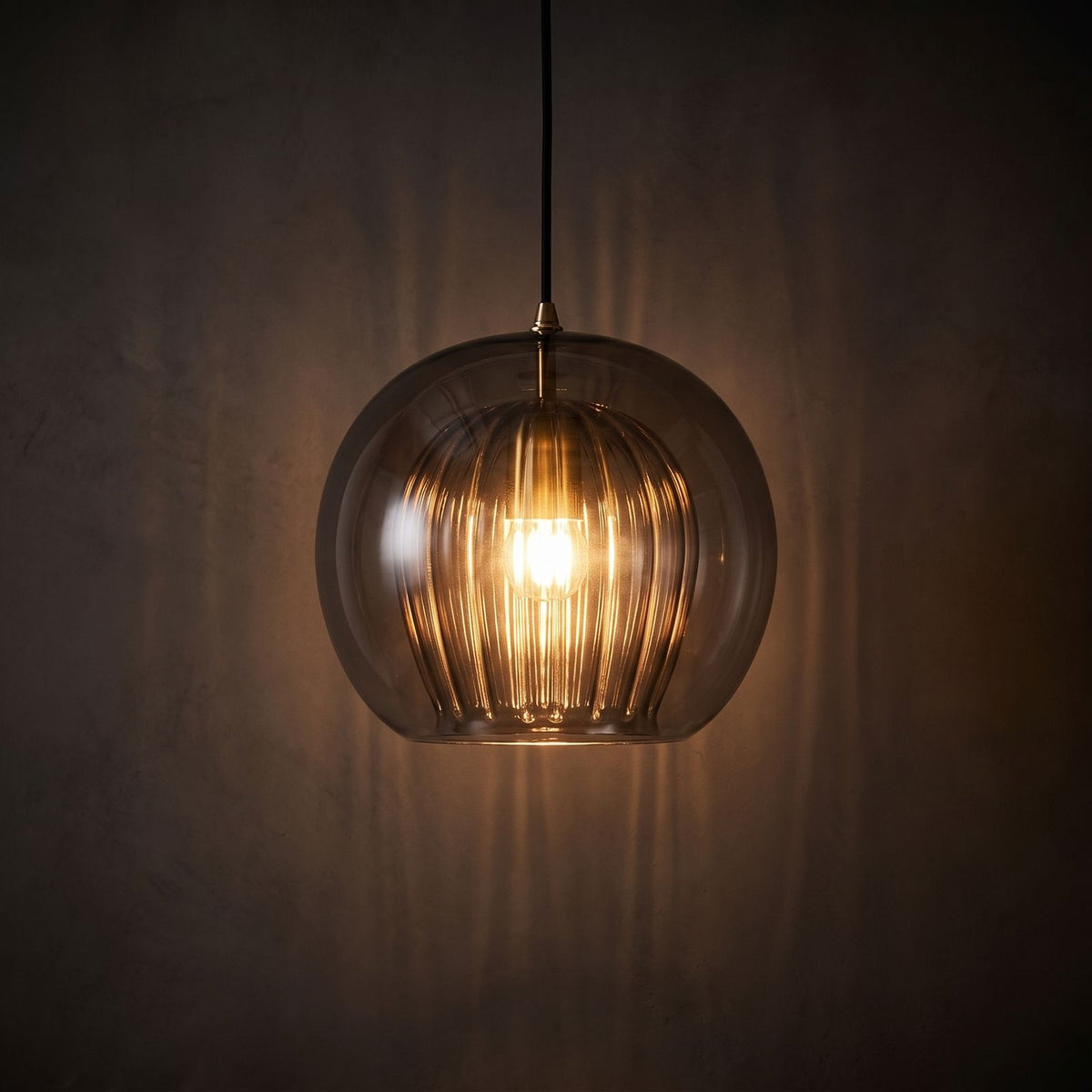 Ribbed Glass Globe Pendant Light glowing against a plaster wall at night