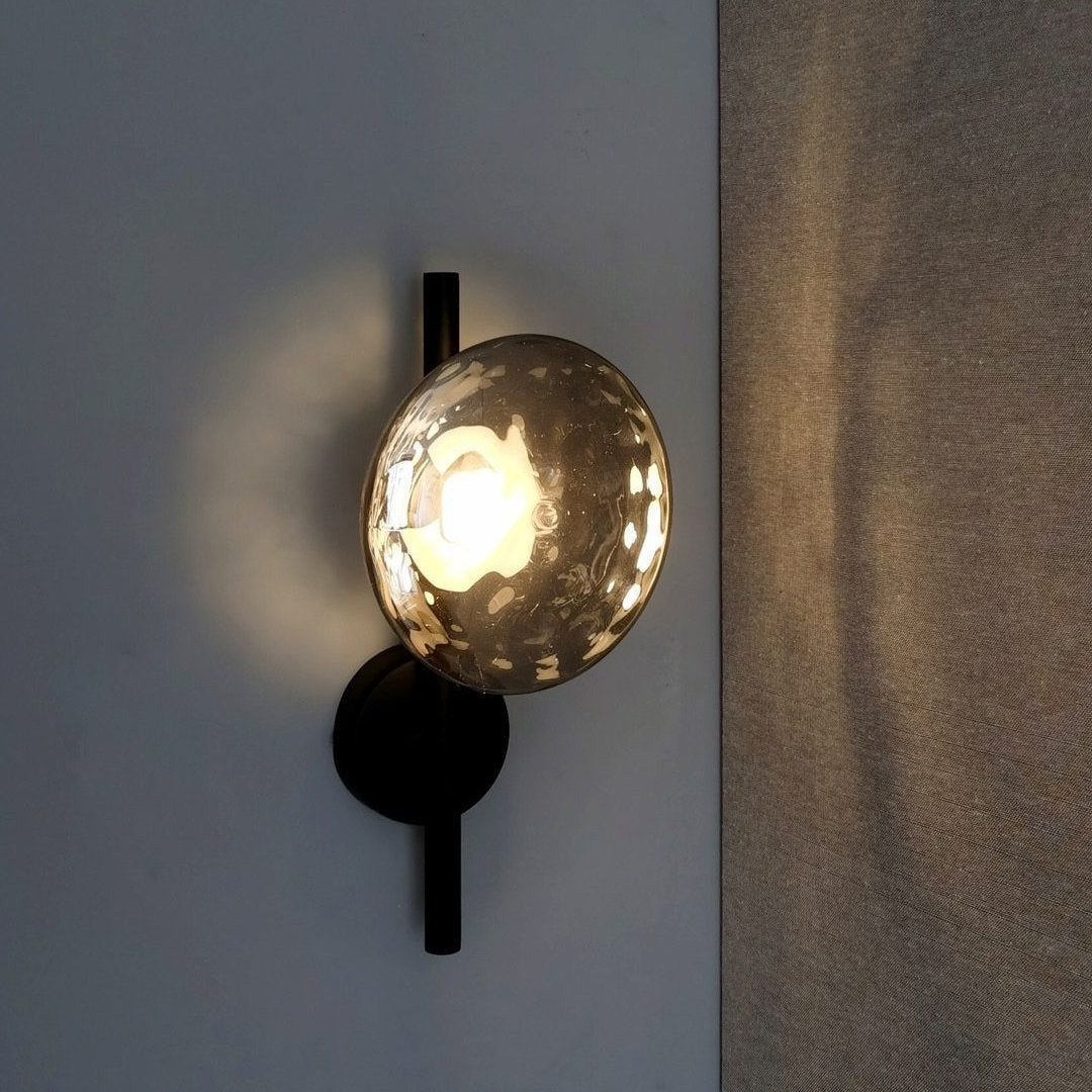 Smoked glass disc wall light glowing on a dark blue wall