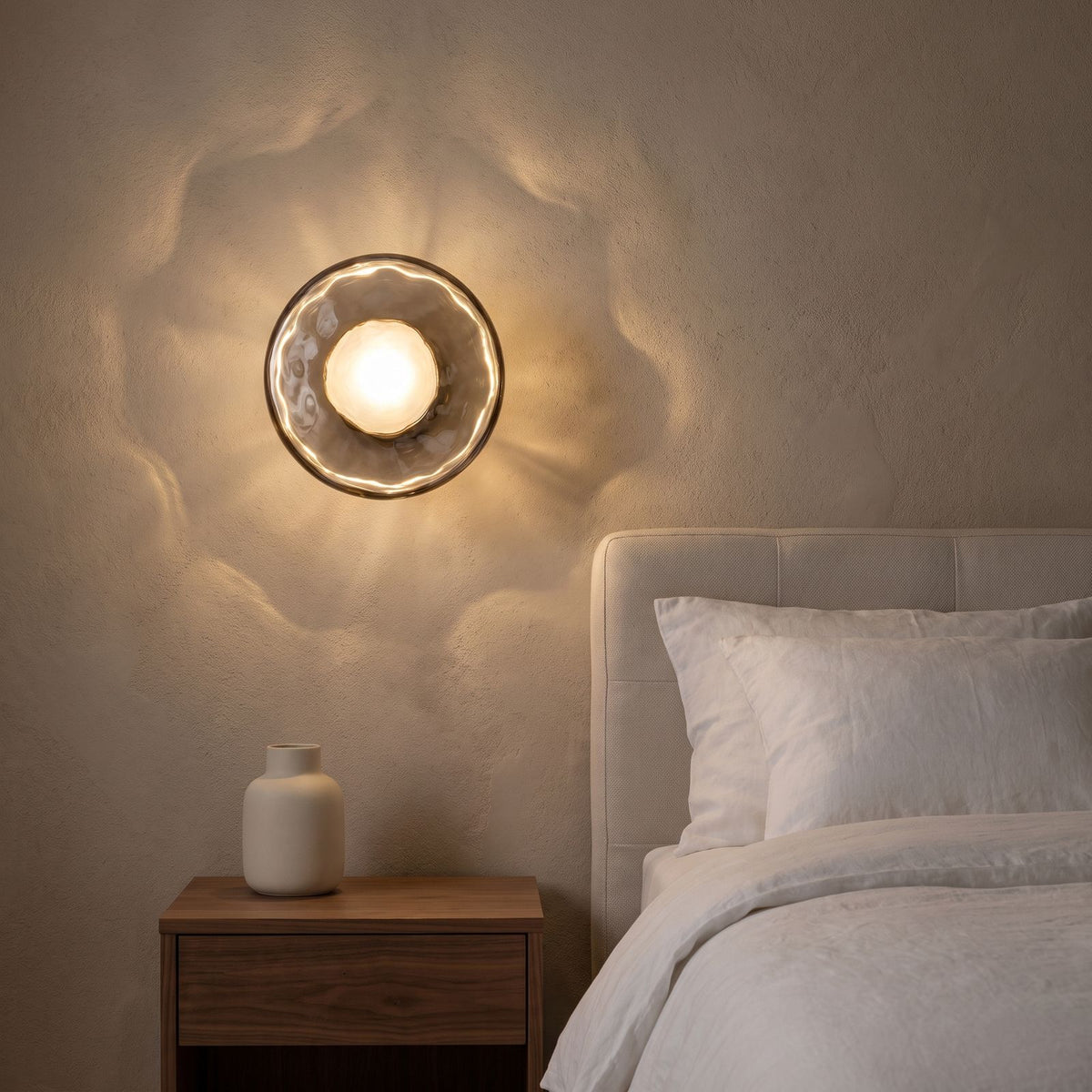 Rippled Smoked Glass Disc Wall Light beside a bed at night