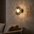 Rippled Smoked Glass Disc Wall Light on a limewashed wall at night
