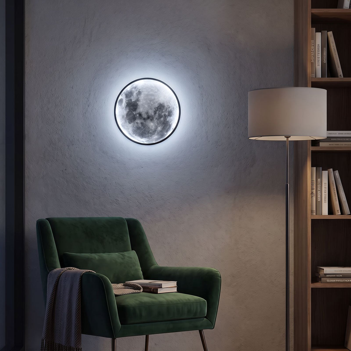Round 3D Moon Black Frame LED Wall Light in cool white beside a velvet armchair in a reading nook at night