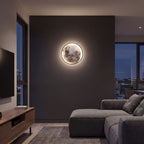 Round 3D Moon Black Frame LED Wall Light in warm white on a dark feature wall in a media room at night