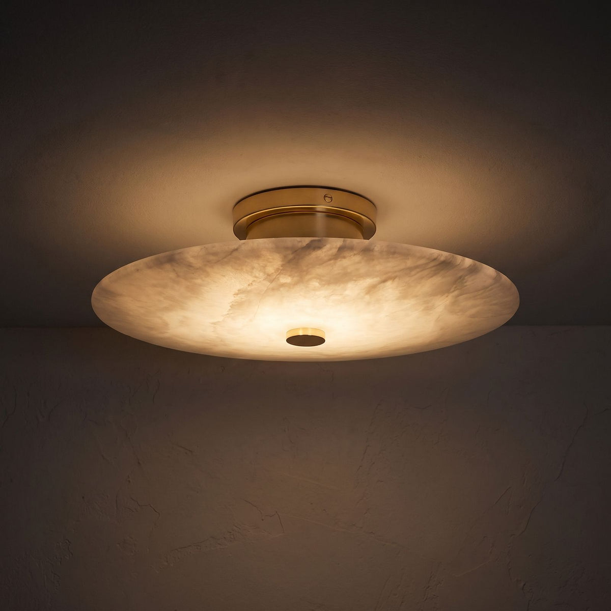 Round Alabaster Flush Wall and Ceiling Light glowing on a plaster wall at night