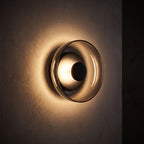Round Glass Dish LED Wall Light glowing on a plaster wall at night