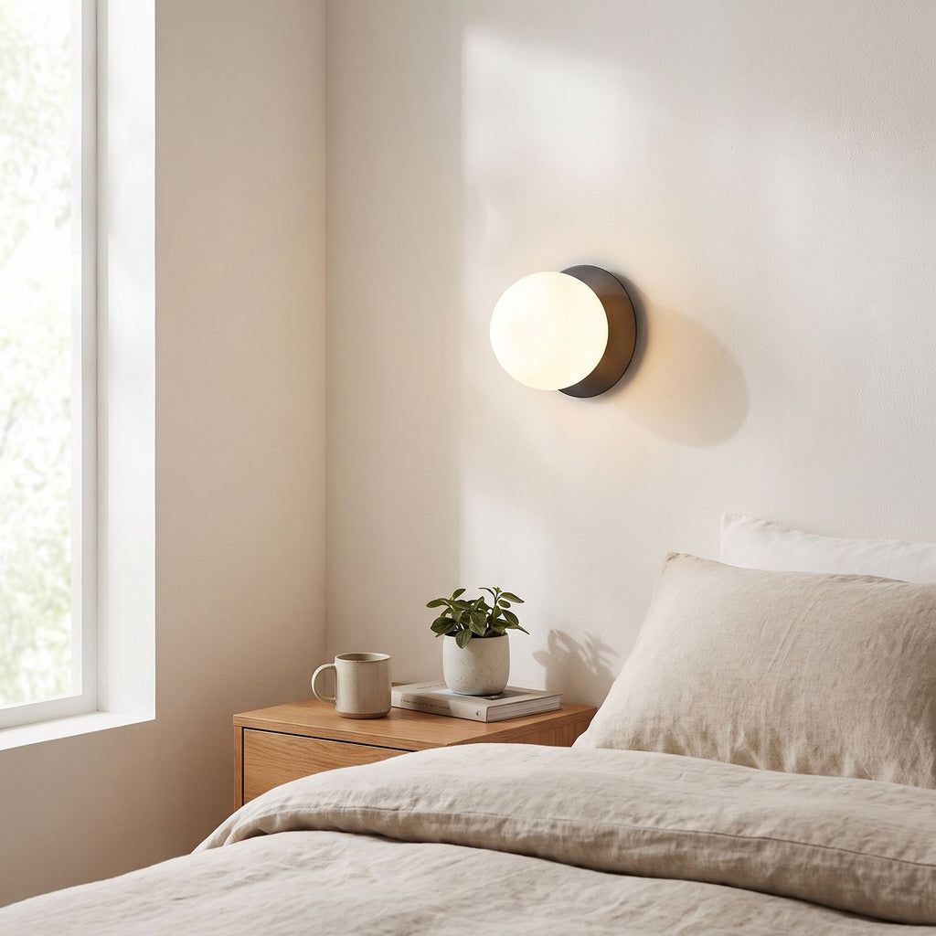 Round Glass Wall Sconce with Metal Backplate on a bedroom wall beside the bed