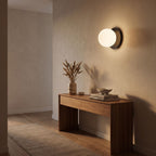 Round Glass Wall Sconce with Metal Backplate in a hallway above a timber console
