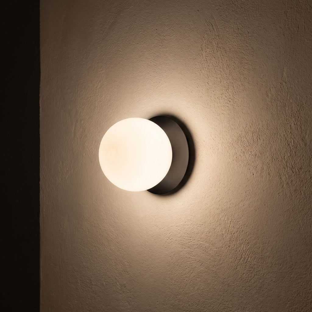 Round Glass Wall Sconce with Metal Backplate glowing on a plaster wall at night