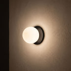 Round Glass Wall Sconce with Metal Backplate glowing on a plaster wall at night