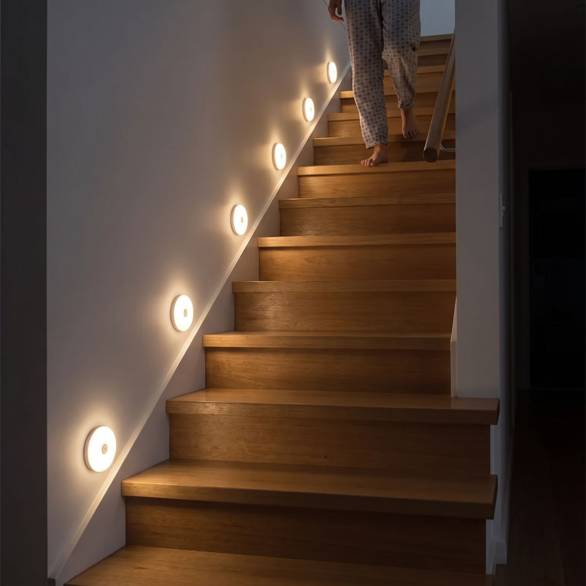 Six round motion sensor lights glowing warm white beside the steps of a timber staircase at night