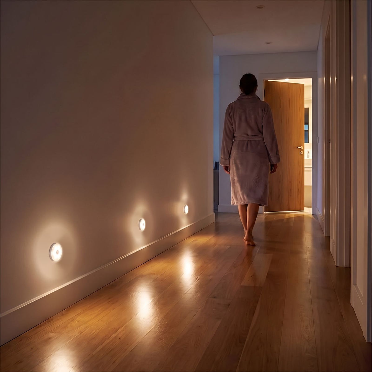 Three round motion sensor lights low on a hallway wall lighting the way to the bathroom at night