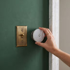 Hand placing the round motion sensor light onto its magnetic plate beside a brass light switch on a green plaster wall