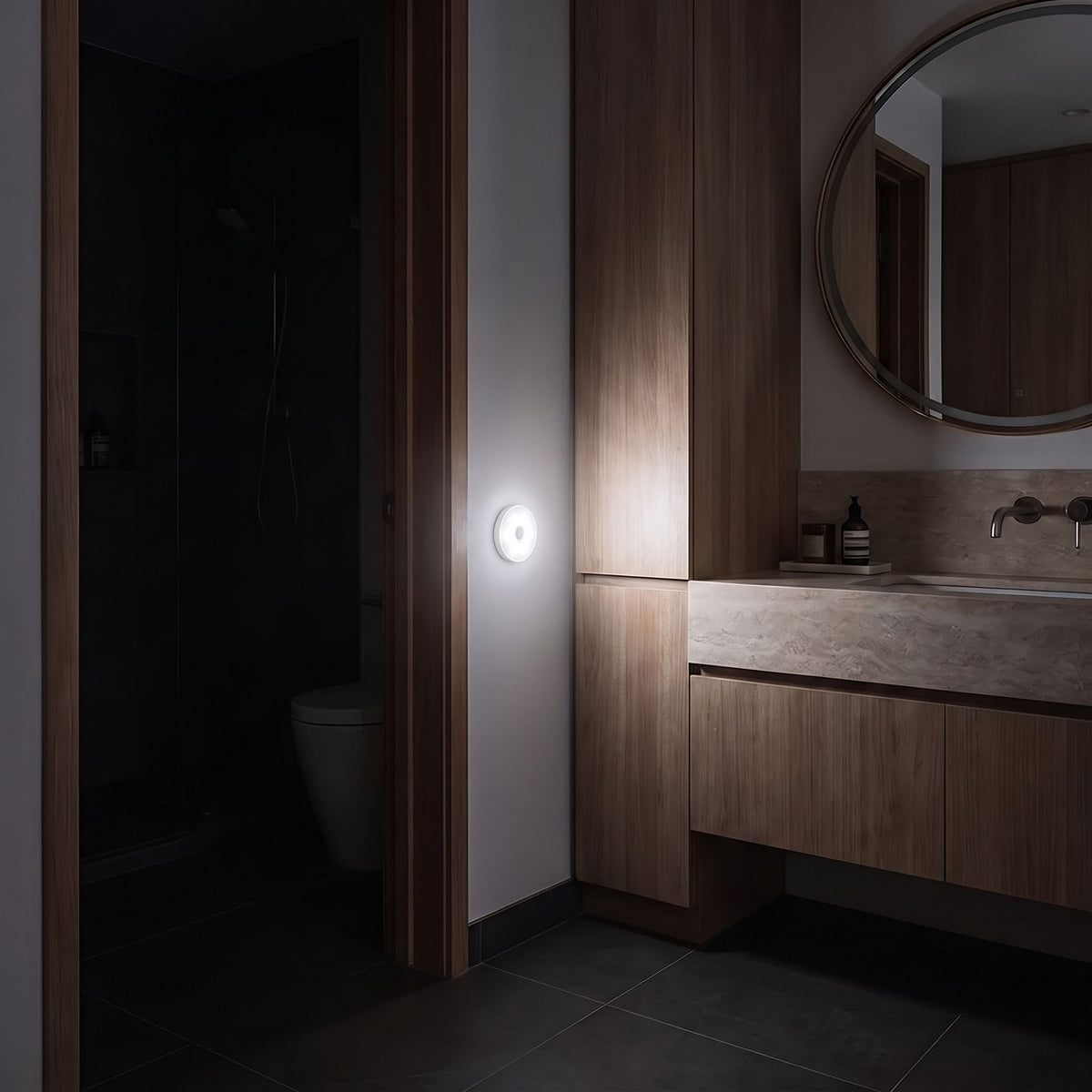 Round motion sensor light glowing white on a bathroom wall beside the door at night