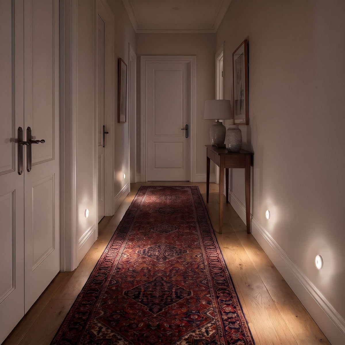 Four round motion sensor lights low on the walls of an upstairs hallway with bedroom doors at night