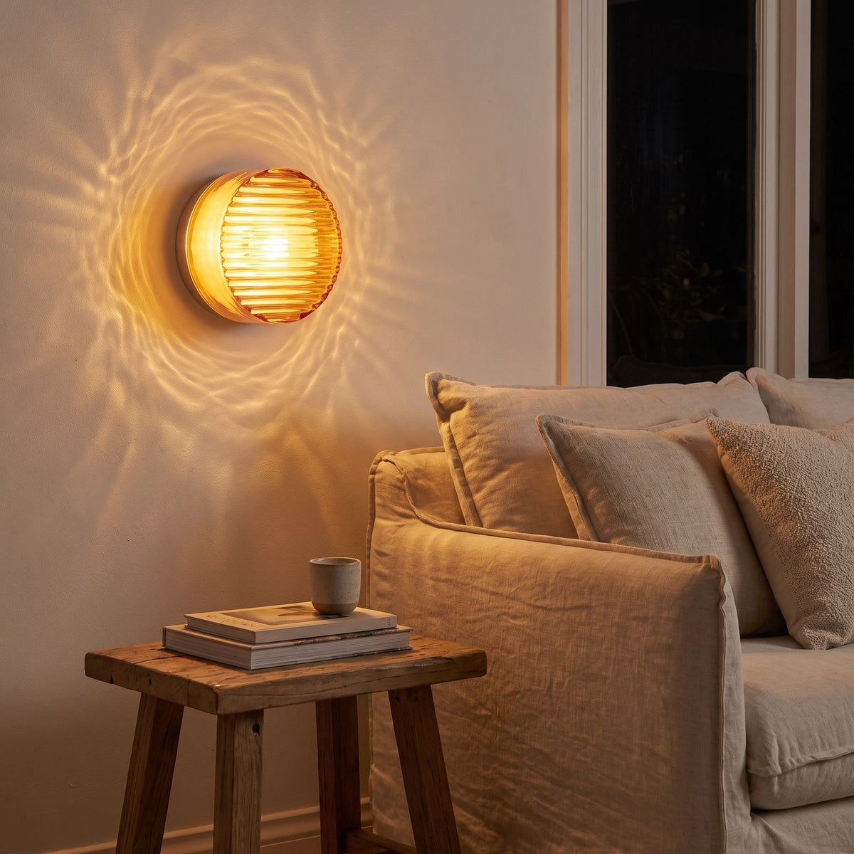 Round ribbed amber glass wall light beside a living room sofa at night