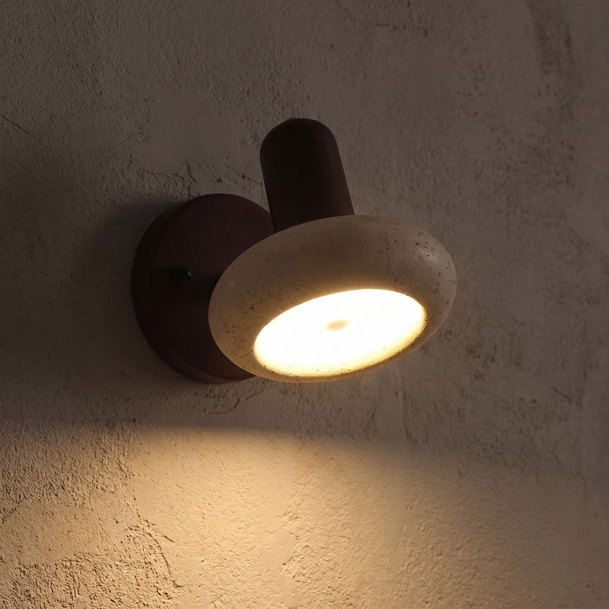 Round Travertine Swivel Bedside Wall Light glowing on a plaster wall at night