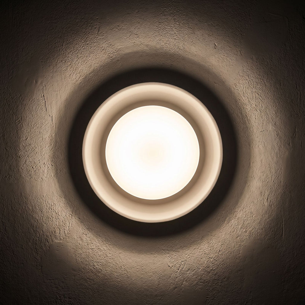 Round White Gypsum and Acrylic Wall Light glowing on a plaster wall at night