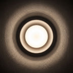 Round White Gypsum and Acrylic Wall Light glowing on a plaster wall at night