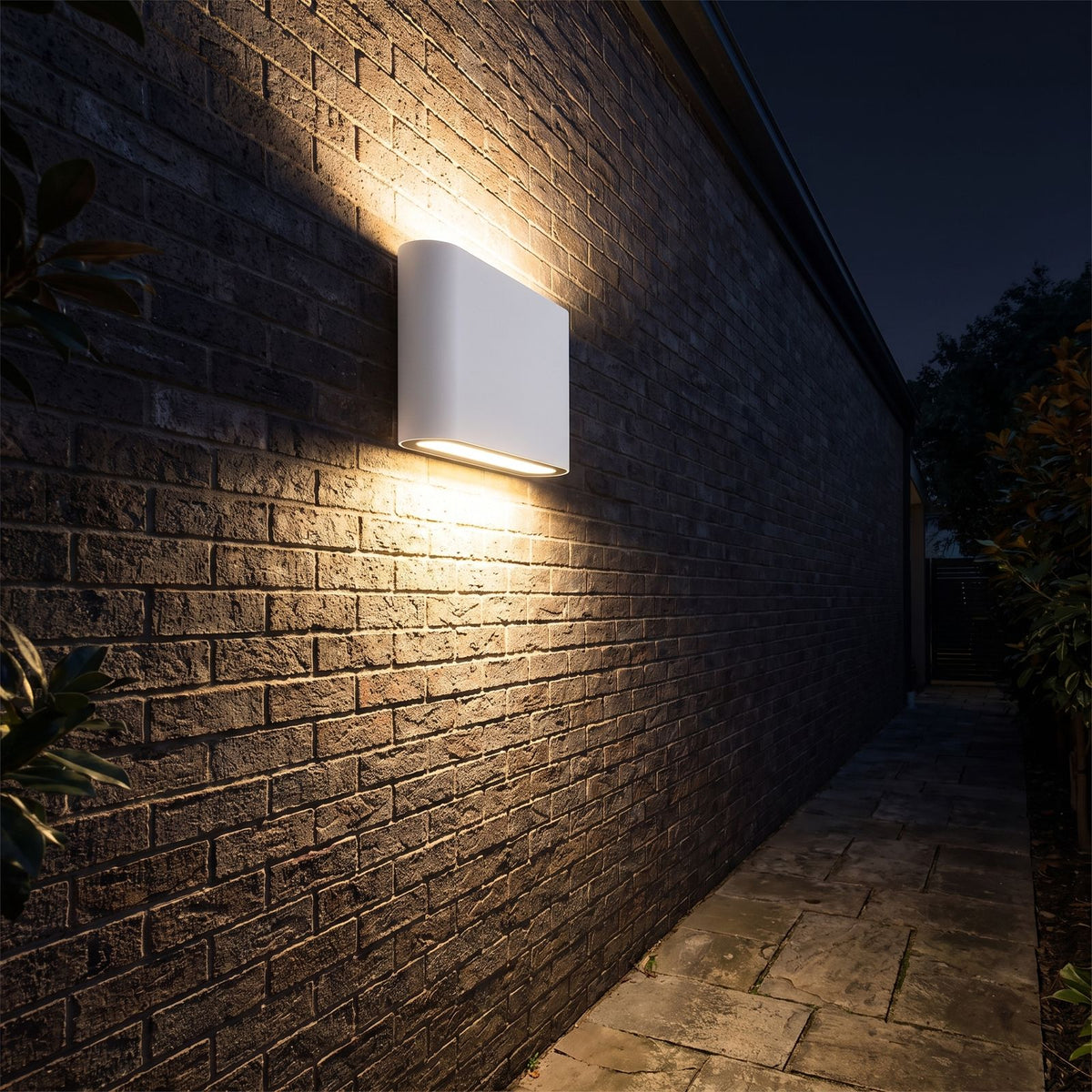 Rounded box up down outdoor wall light along a side passage at night
