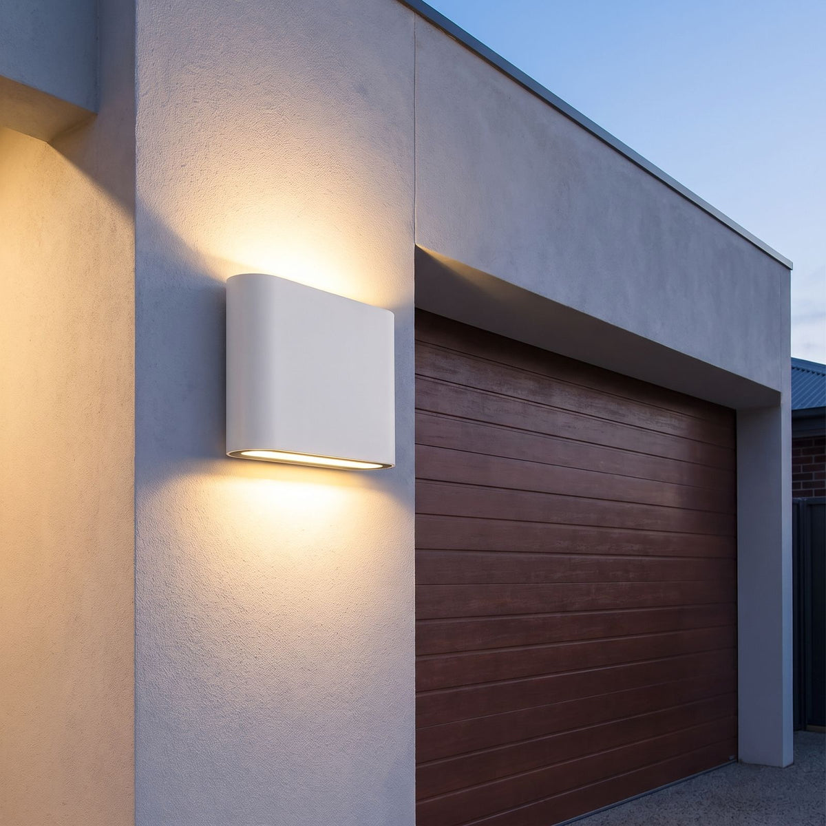 Rounded box up down outdoor wall light beside a garage door at dusk