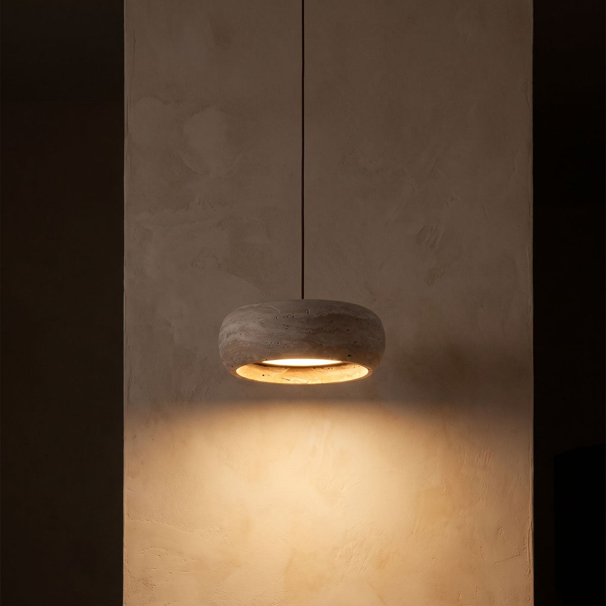 Rounded Travertine Puck LED Pendant Light glowing against a plaster wall at night