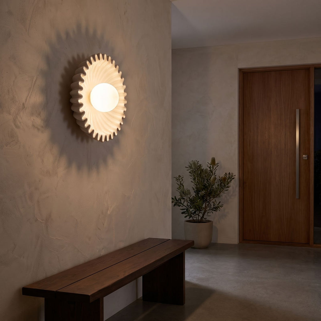 Ruffled ceramic flower wall light beside a round mirror in an entry hall at night