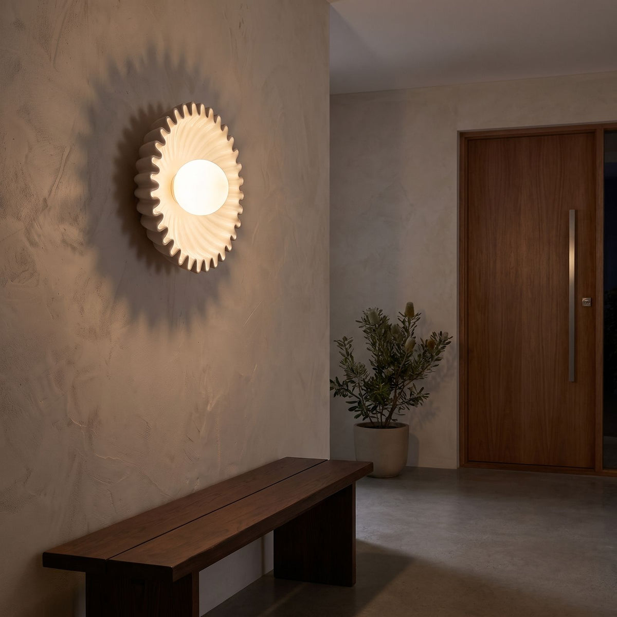 Ruffled ceramic flower wall light beside a round mirror in an entry hall at night
