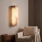 Scalloped alabaster half-cylinder wall sconce above an armchair in a reading corner