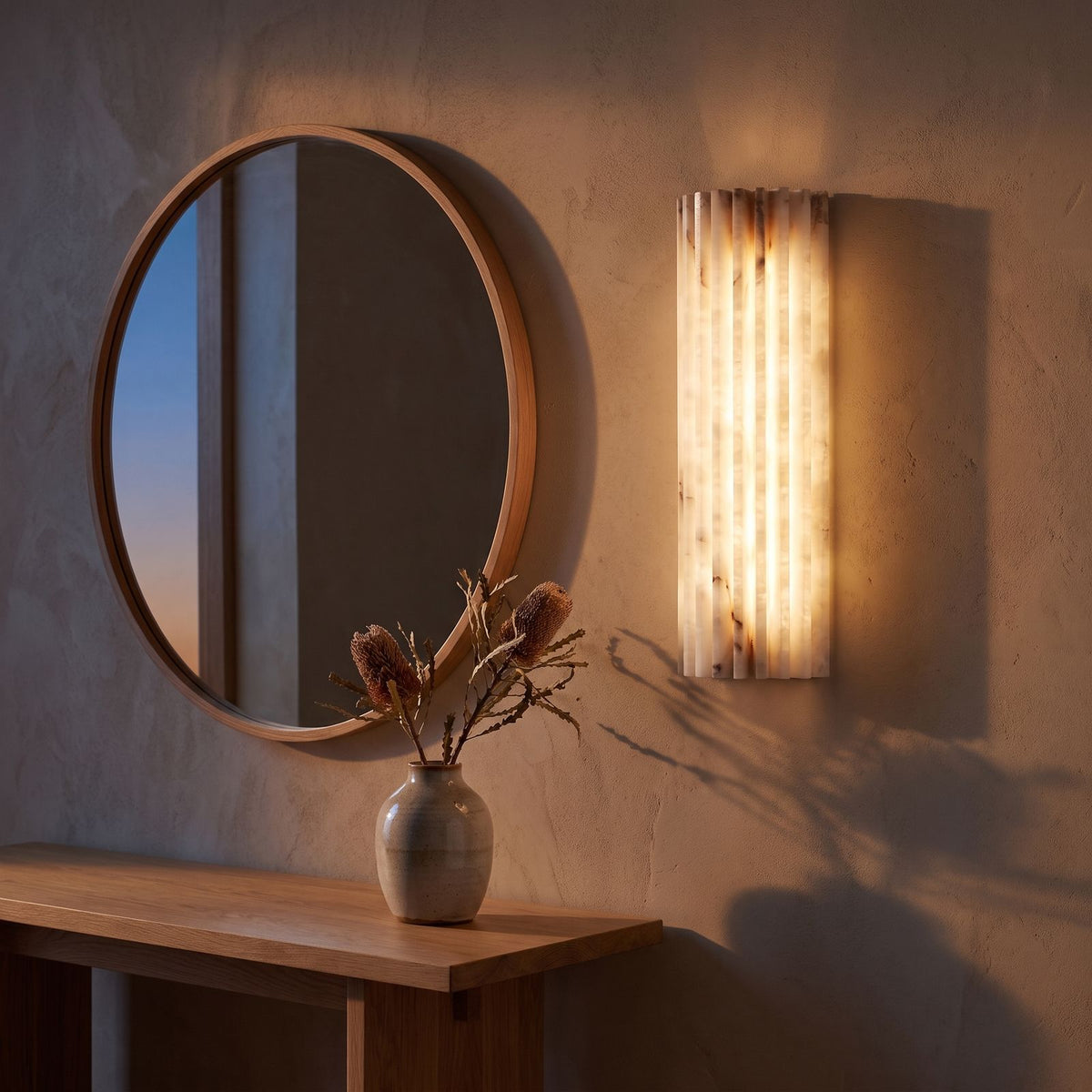 Scalloped alabaster half-cylinder wall sconce beside a round mirror in an entry hall