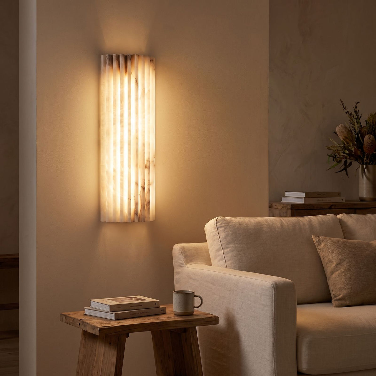 Scalloped alabaster half-cylinder wall sconce beside a living room sofa at night