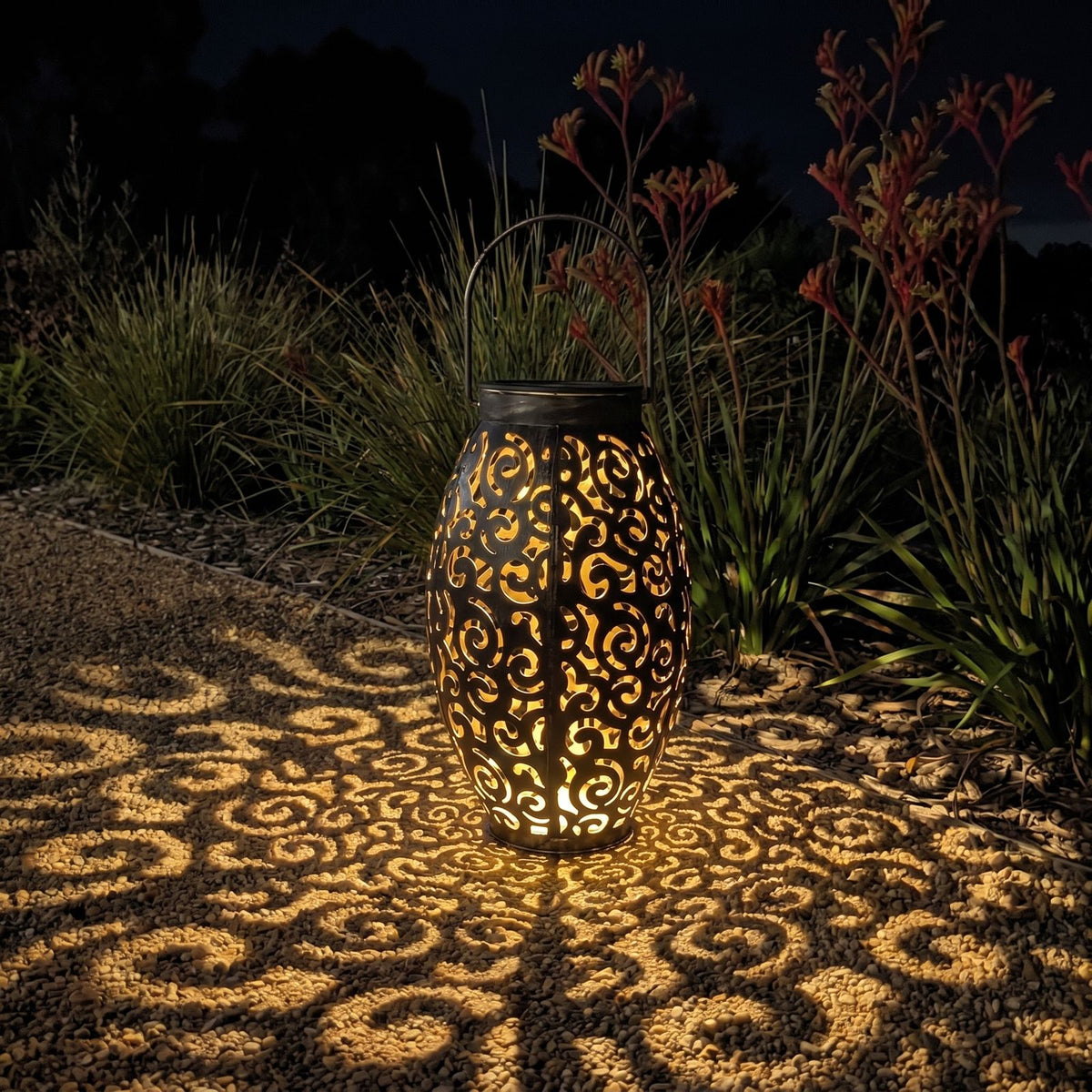 Scroll pattern metal solar lantern beside a gravel garden path at night