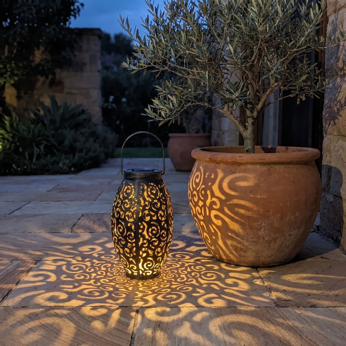 Scroll pattern metal solar lantern in a paved courtyard at night