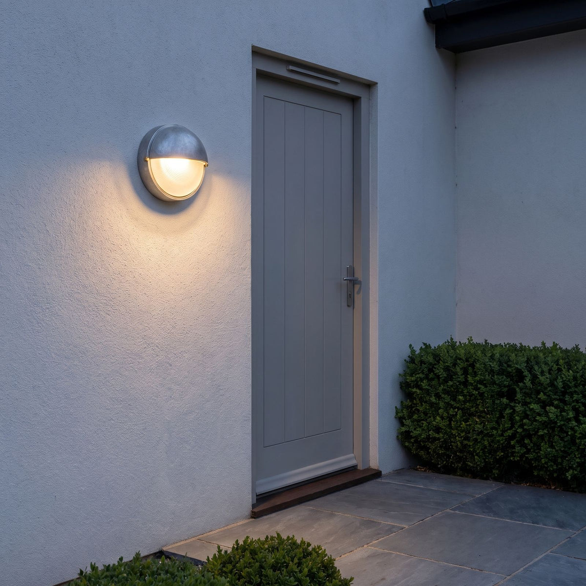 Silver Bulkhead Outdoor Wall Light beside a side door on a rendered wall
