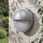 Silver Bulkhead Outdoor Wall Light on a painted brick wall, angled close view