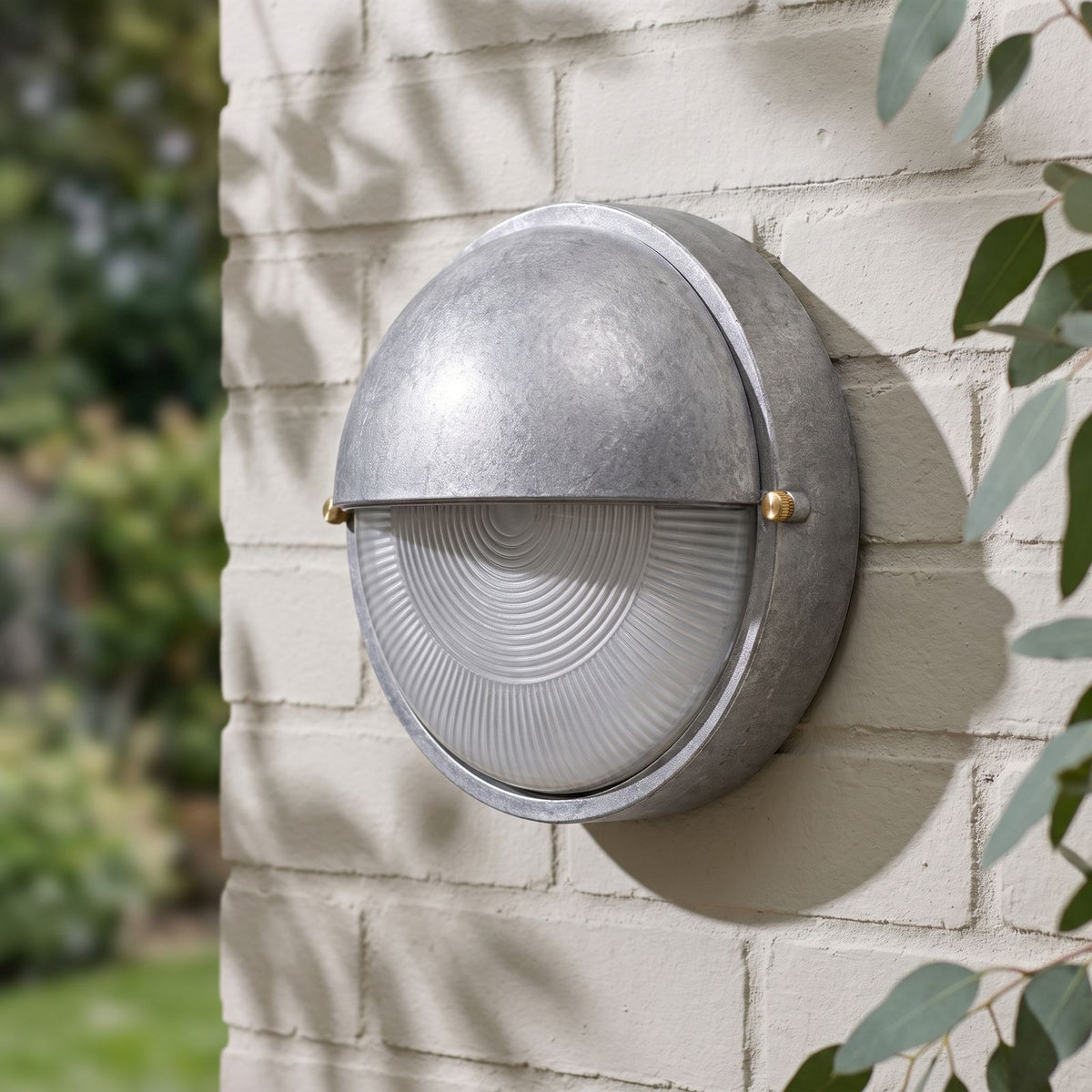 Silver Bulkhead Outdoor Wall Light on a painted brick wall, angled close view