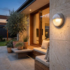 Silver Bulkhead Outdoor Wall Light on a limestone wall beside an outdoor lounge