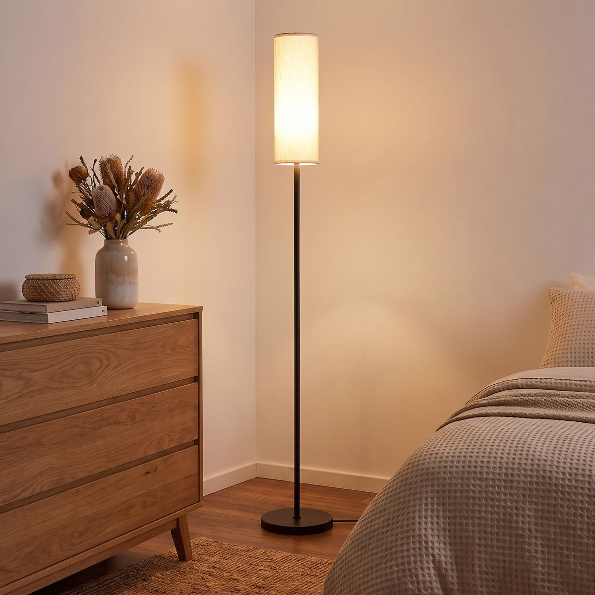 Fabric cylinder shade floor lamp in a bedroom corner beside a dresser